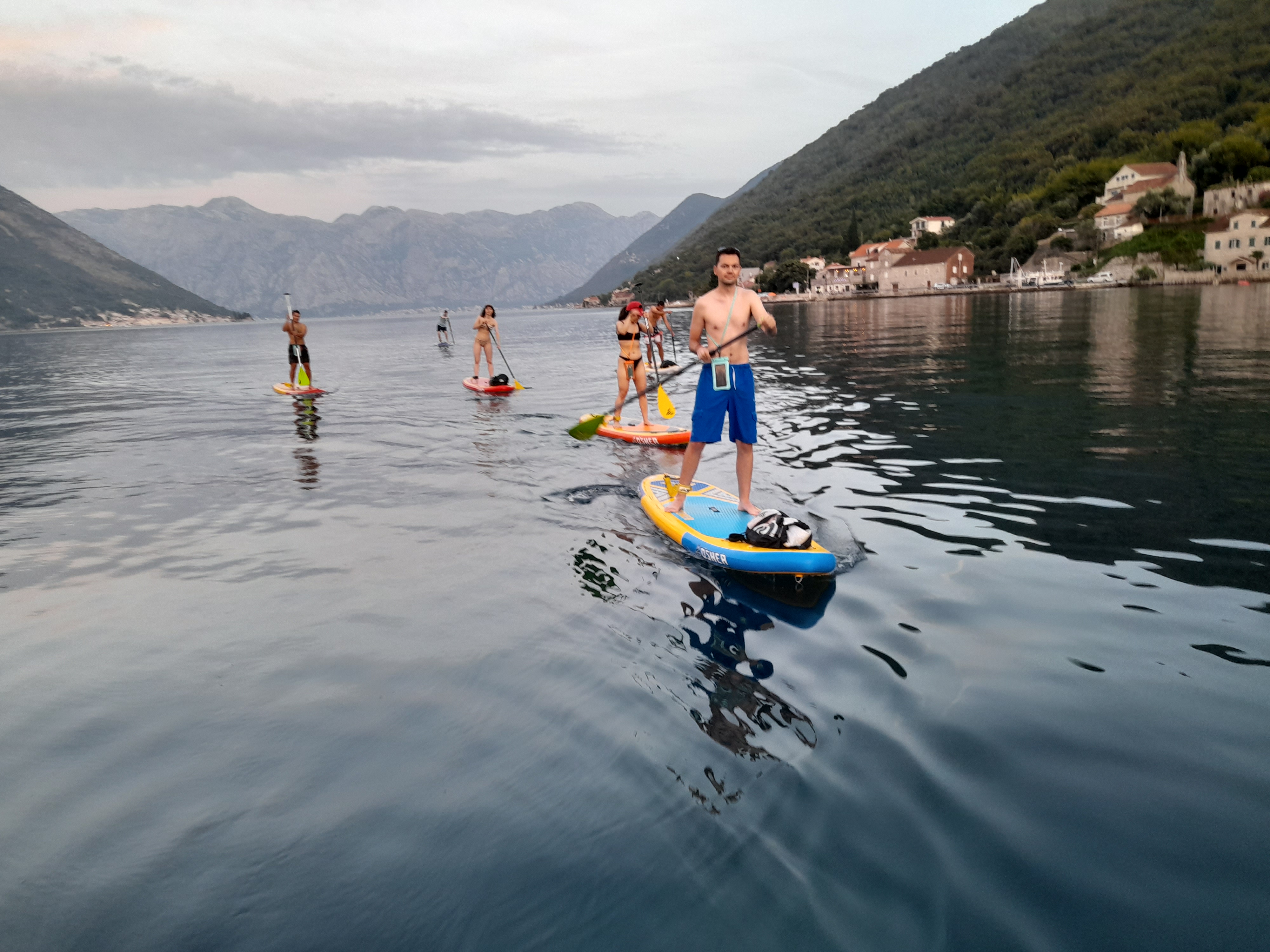 Group of paddleboarders on evening water with Perast village backdrop