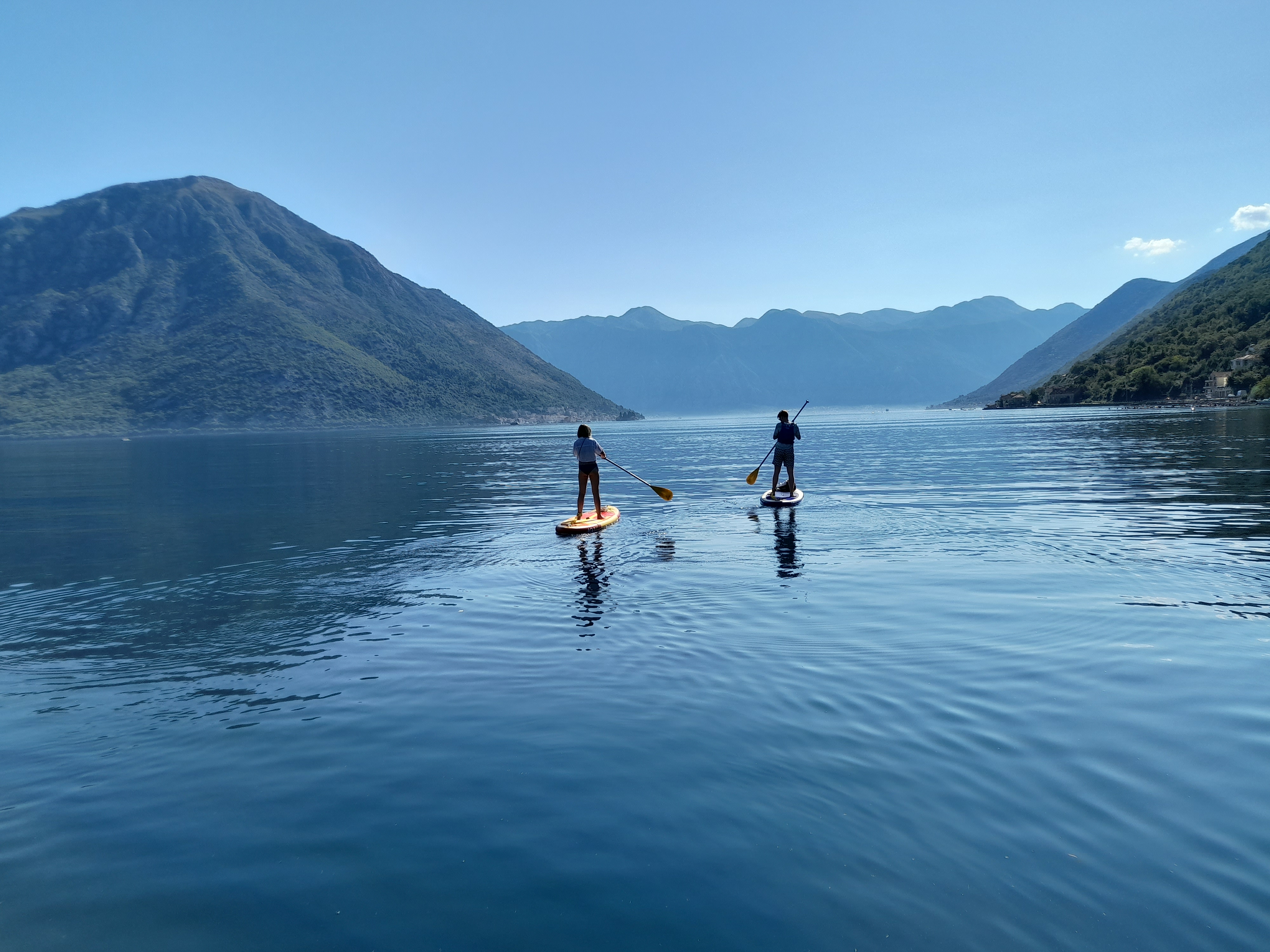 Two paddleboarders on calm bay with mountain panorama