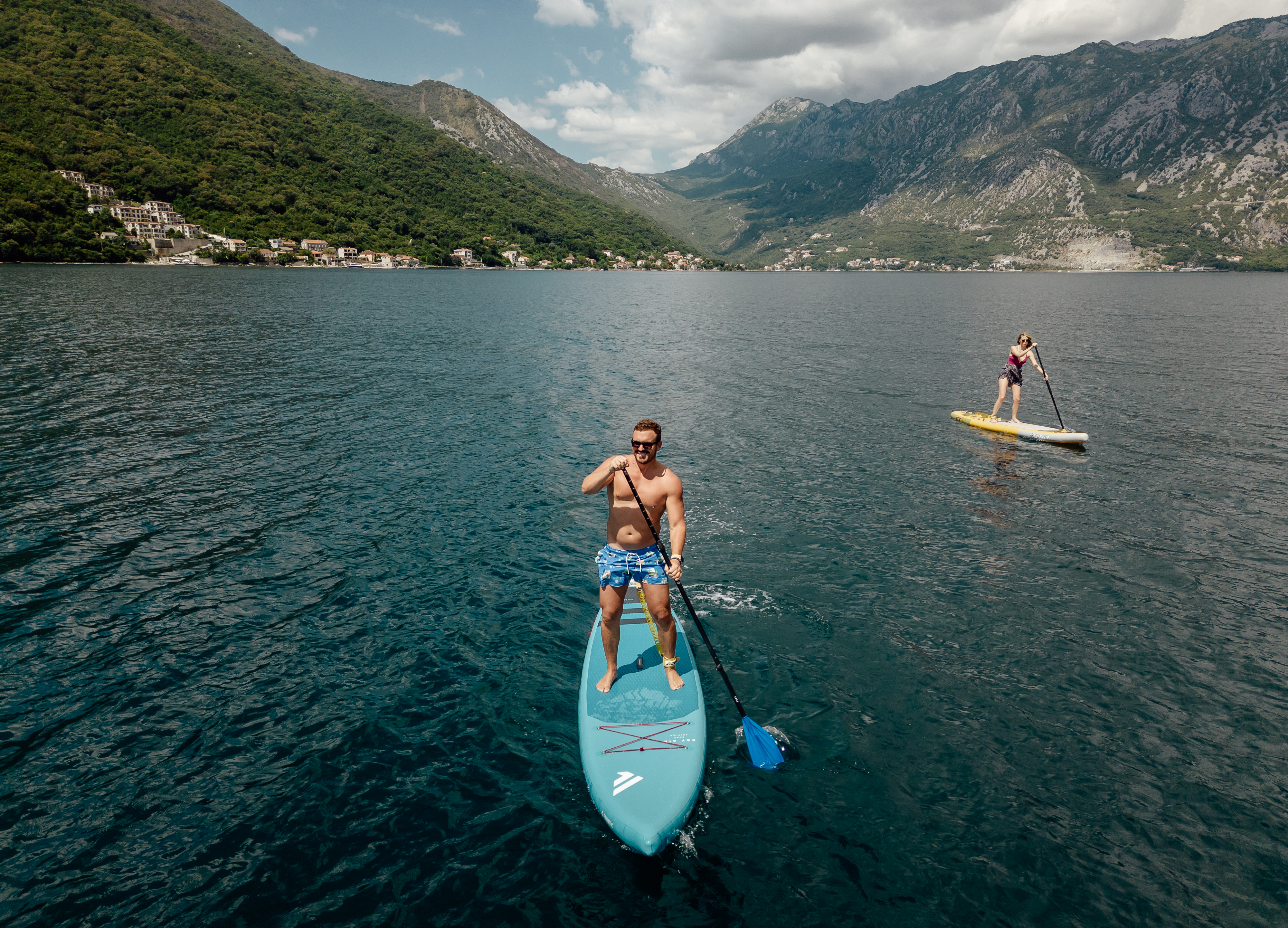 Two paddleboarders from above on sunlit deep-blue water
